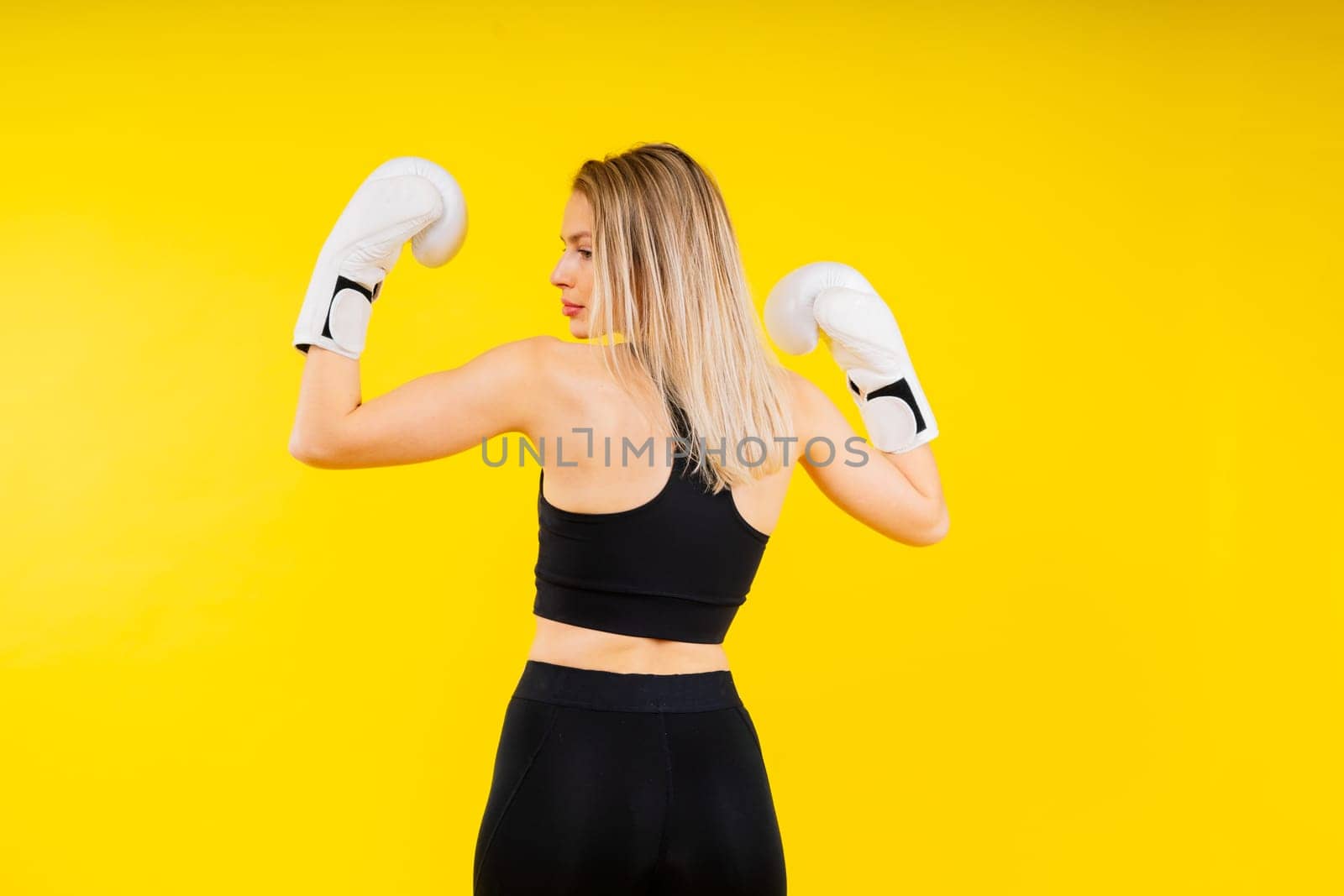 Woman boxer in gloves training on a yellow and dark studio background