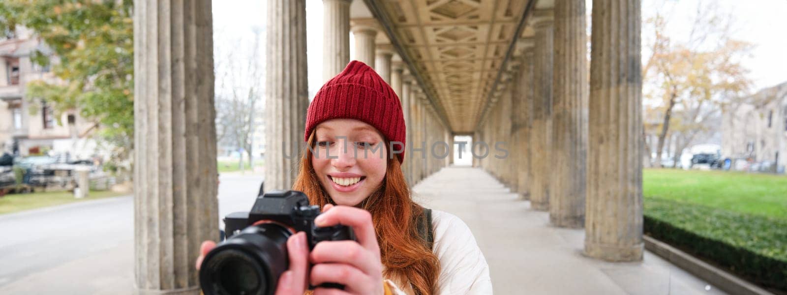 Smiling tourist photographer, takes picture during her trip, holds professional camera and makes photos. Copy space