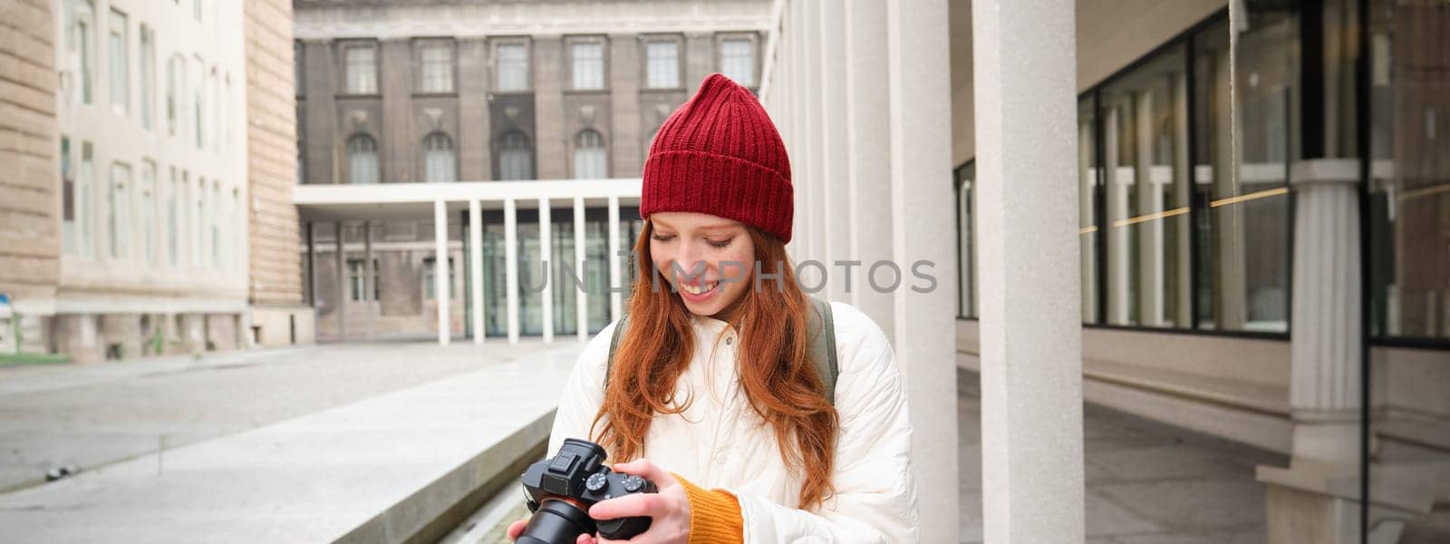 Beautiful readhead girl, photographer with professional camera takes pictures outdoors, walking around city and taking photos, sightseeing.