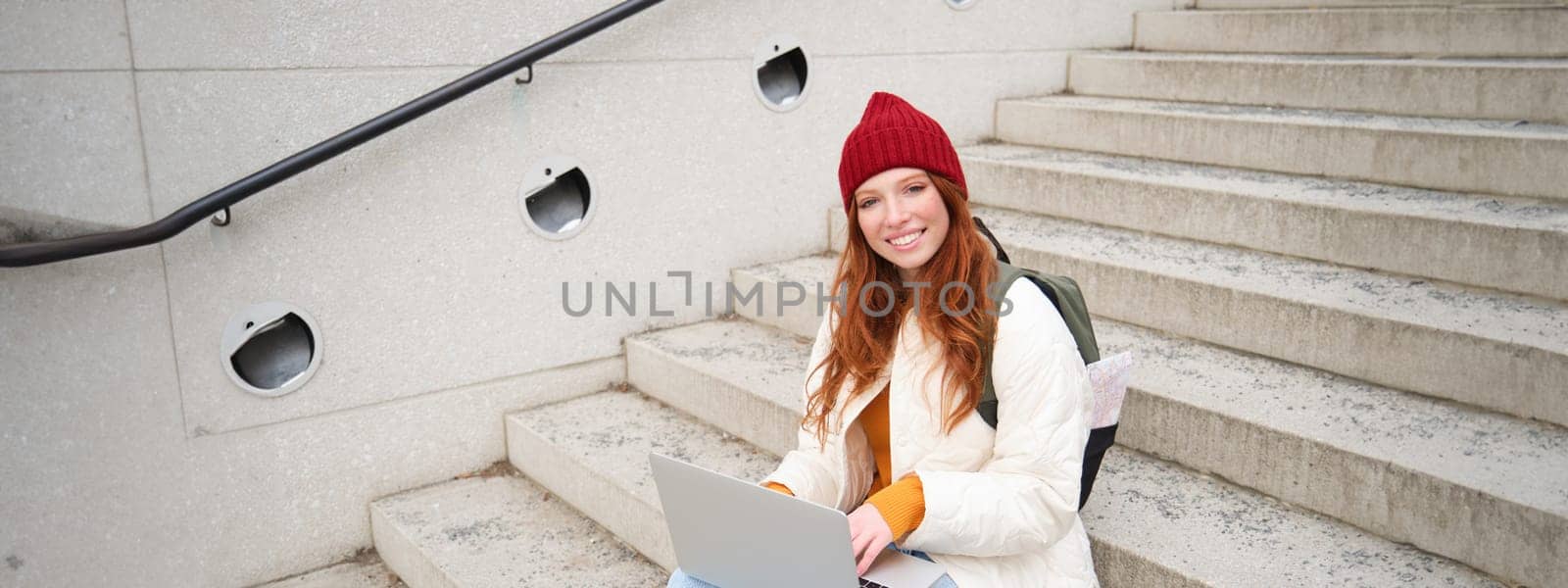 Portrait of young girl traveller, sitting with backpack and map of city, working on laptop, connecting to public wifi and sitting on stairs outdoors, using internet to book hotel room by Benzoix