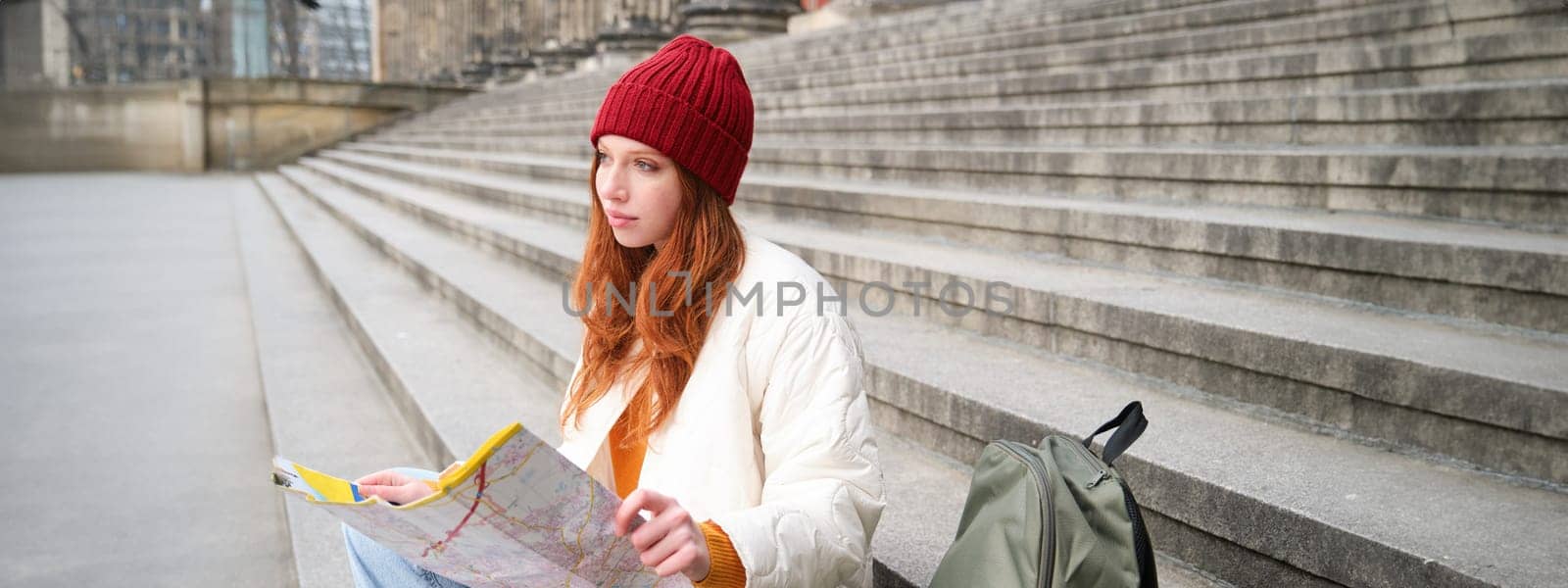 Beautiful young woman, traveler with backpack holds paper map, explores city sightseeing, plans route for tourism popular attractions by Benzoix