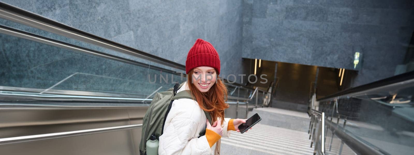 Smiling girl walking on stairs, using mobile phone, texting message on her way, using smartphone app map, follows route to destination place.