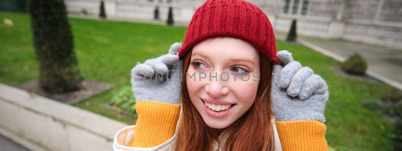 Cute girl student in red hat, warm gloves, sits in park, smiles and looks happy. Copy space