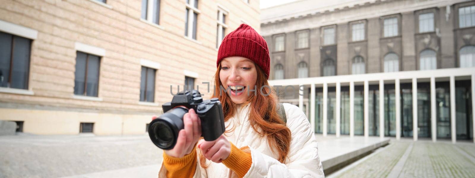 Beautiful readhead girl, photographer with professional camera takes pictures outdoors, walking around city and taking photos, sightseeing by Benzoix