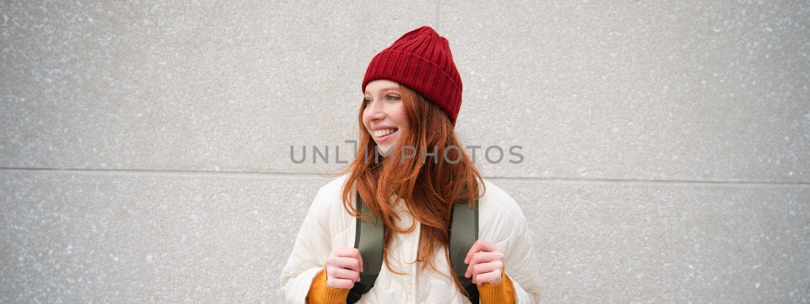 Happy young girl, redhead tourist in red hat with backpack, walks around town, explores city, backpacking around europe, travelling alone.