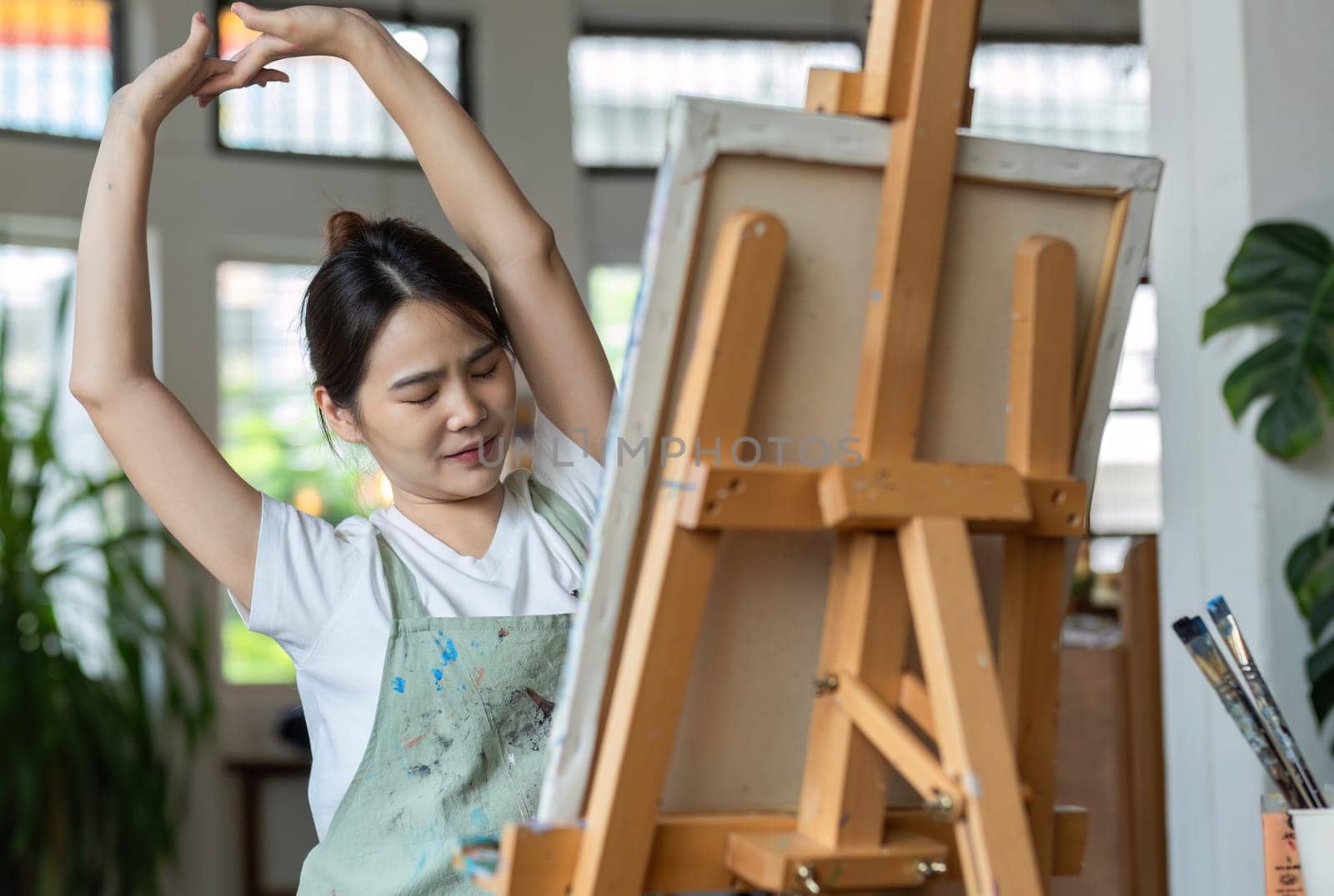 Young woman tired from painting stretches her muscles to relax after sitting and painting for a long time..