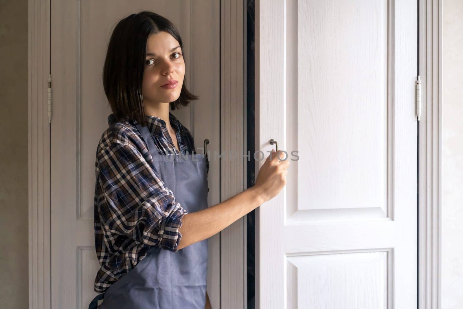 A young girl in casual clothes opens the door of a white wooden cabinet in her light, cozy room.