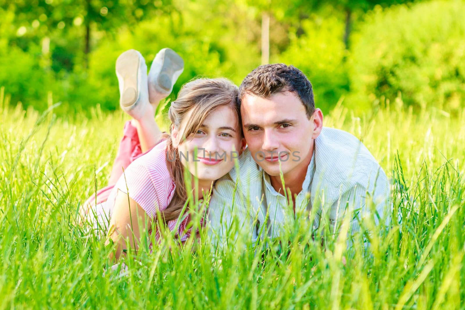 Cheerful young beautiful couple is lying in the field and enjoying the surrounding nature.
