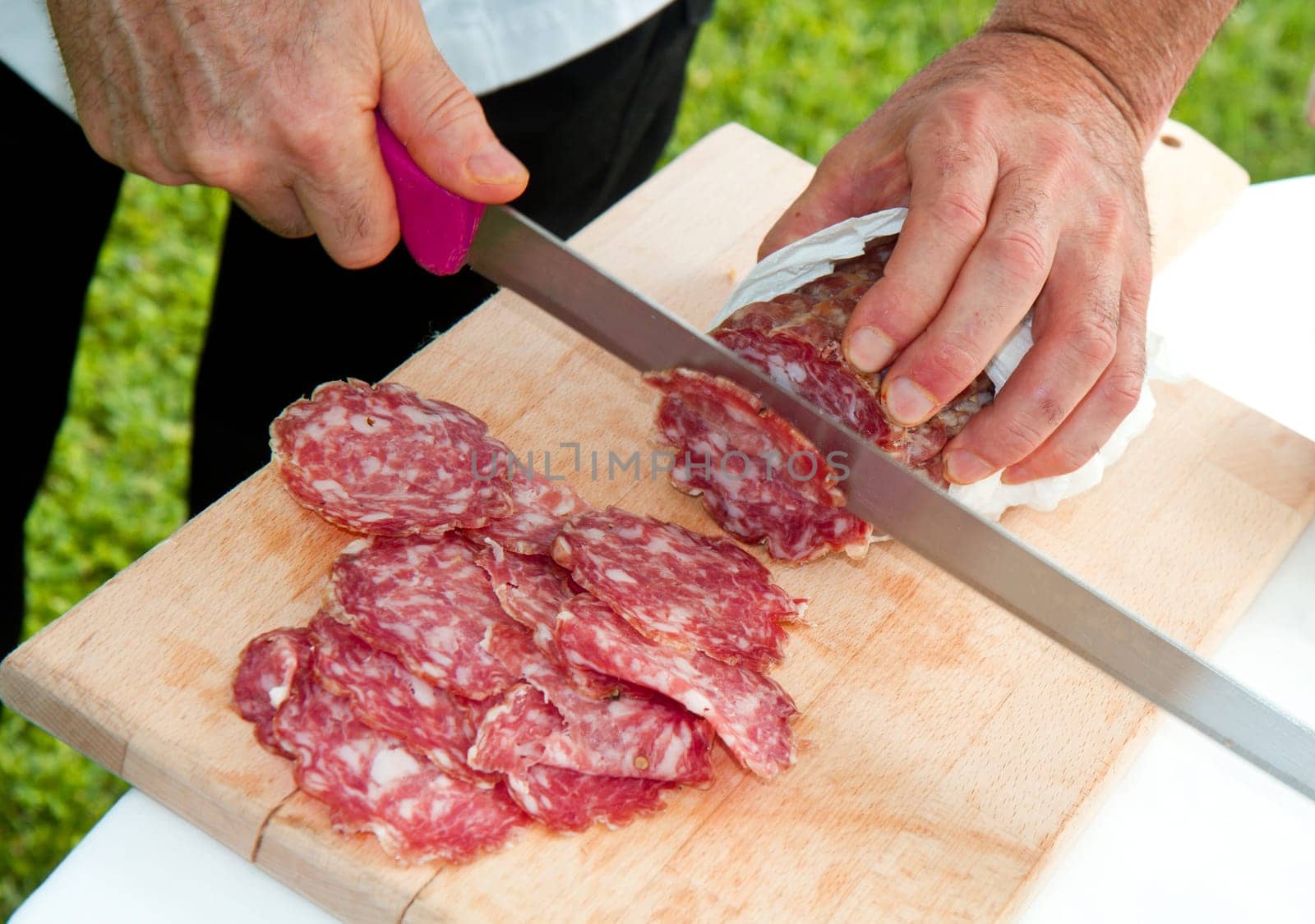 Hand closeup cuts salami with slice pieces at table