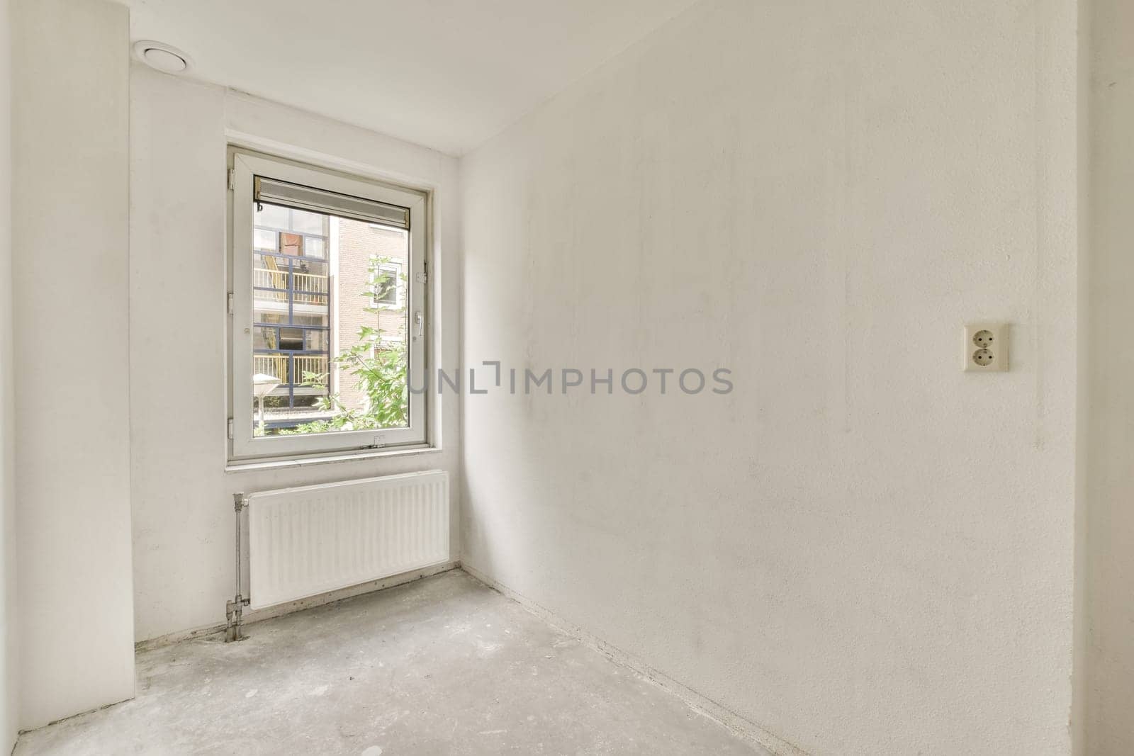 an empty room with white walls and no one person standing in the corner looking out at the view from the window