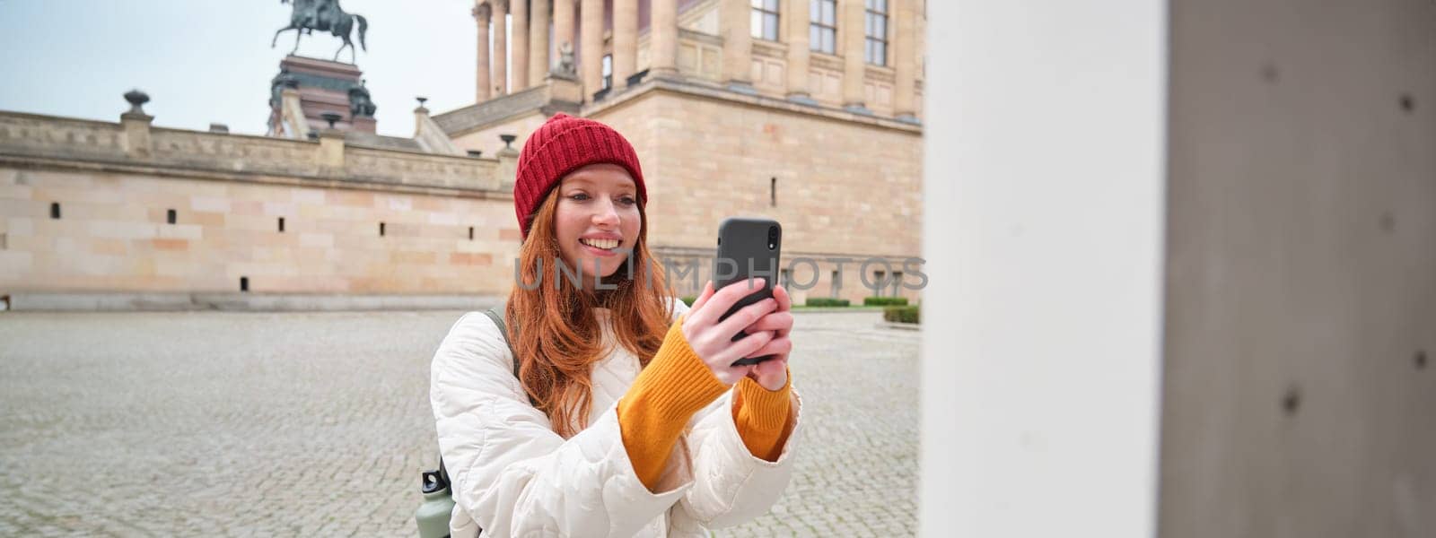 Smiling girl tourist takes photo of historical landmark, makes a photo on smartphone by Benzoix