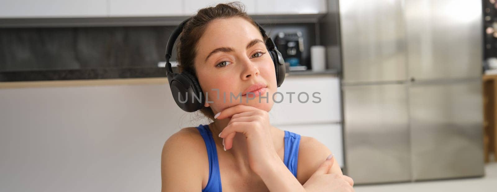 Close up portrait of fitness woman, wearing sportsbra, listening music in headphones, working out at home, doing exercises for fit and healthy body.