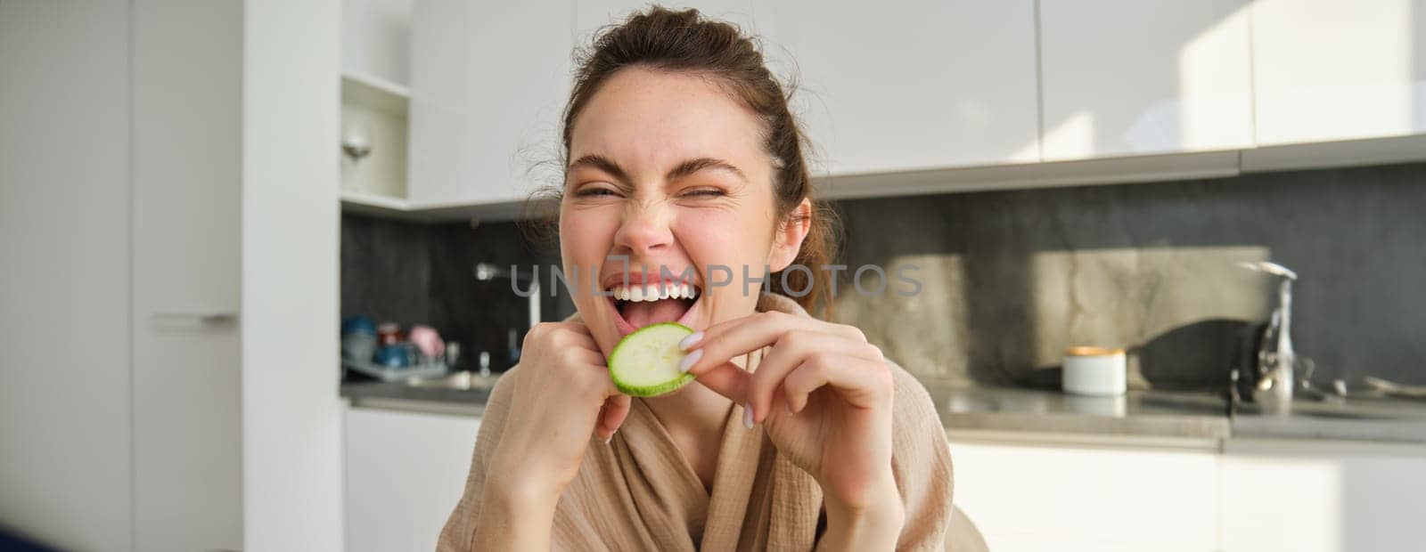 Portrait of happy, smiling young woman in the kitchen, cooking, chopping zucchini, holding vegetables and looking happy, preparing vegan food meal at home.