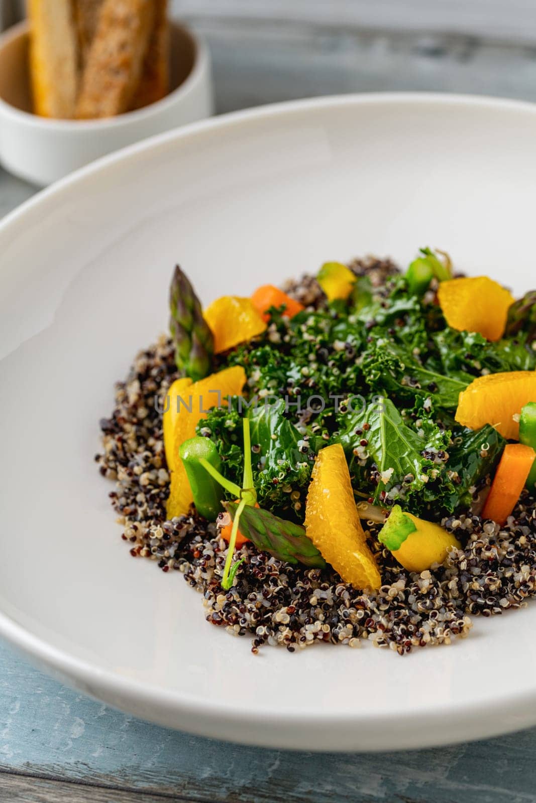 Quinoa salad with orange and kale leaves on white porcelain plate on wooden table by Sonat