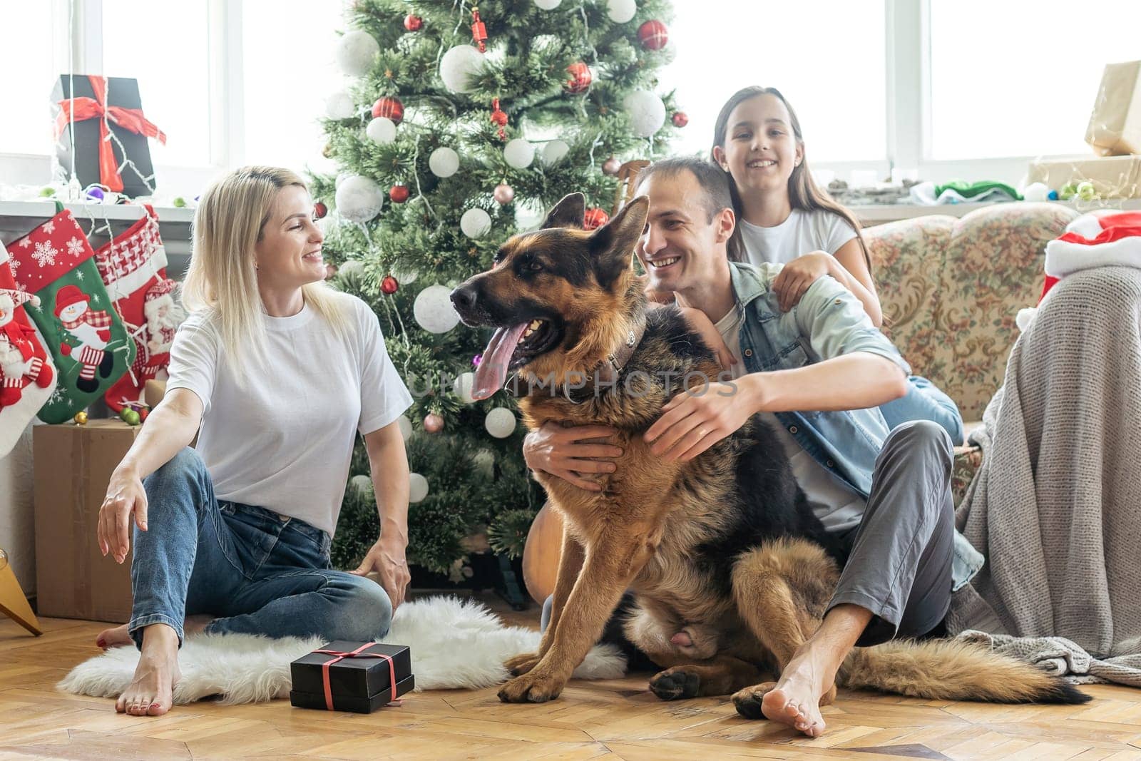 Excited girl and her family sitting on the floor near christmas tree and smiling. family during Christmastime.