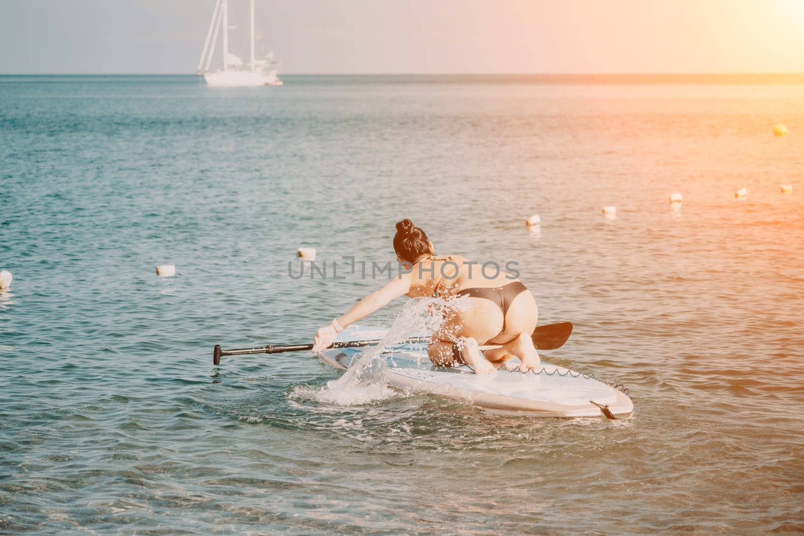 Sea woman sup. Silhouette of happy middle aged tanned woman in rainbow bikini, surfing on SUP board, confident paddling through water surface. Idyllic sunset. Active lifestyle at sea or river. by panophotograph