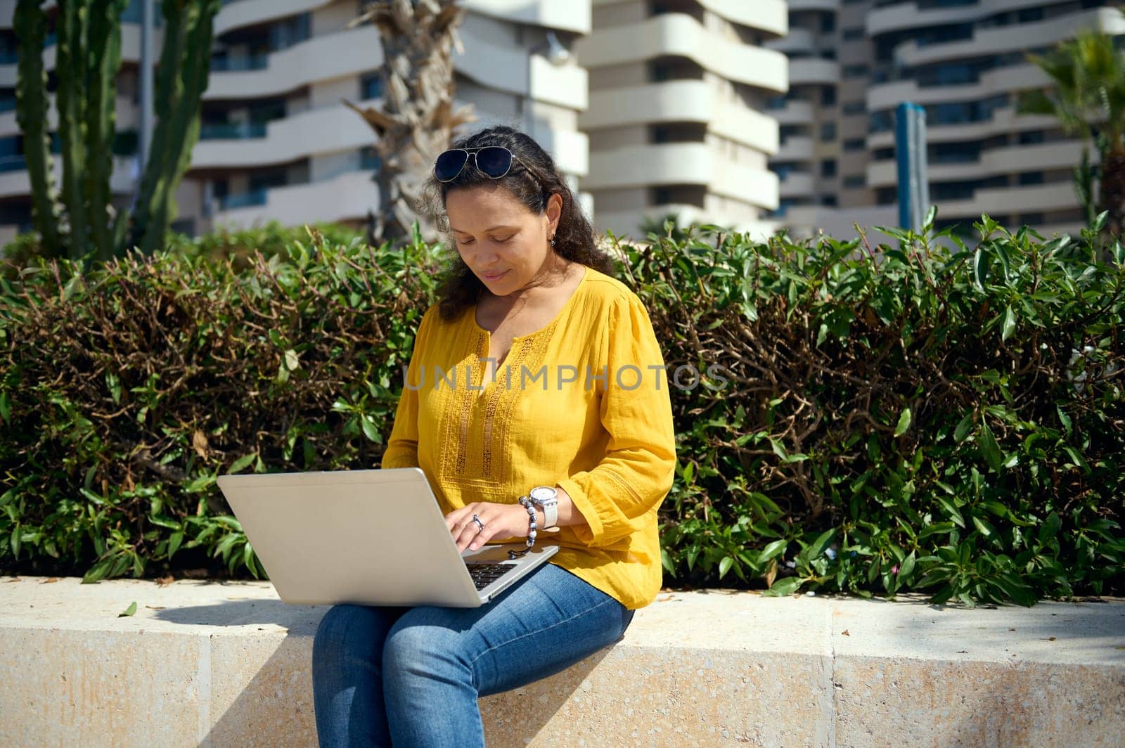 Multiethnic young adult woman dressed in casual clothes, planning start-up, typing text on laptop while telecommuting, working online outdoor. People. Freelance occupation. Remote job. Online business