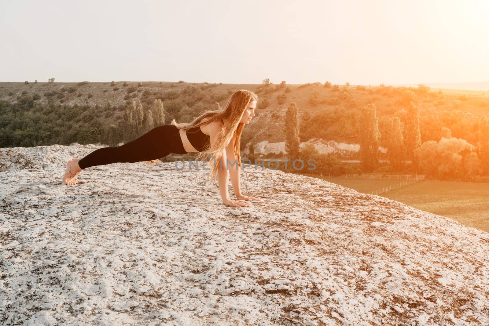 Fitness woman. Happy middle-aged fitness woman doing stretching and pilates on a rock near forest at sunset. Female fitness yoga routine. Healthy lifestyle with focus on well-being and relaxation. by panophotograph