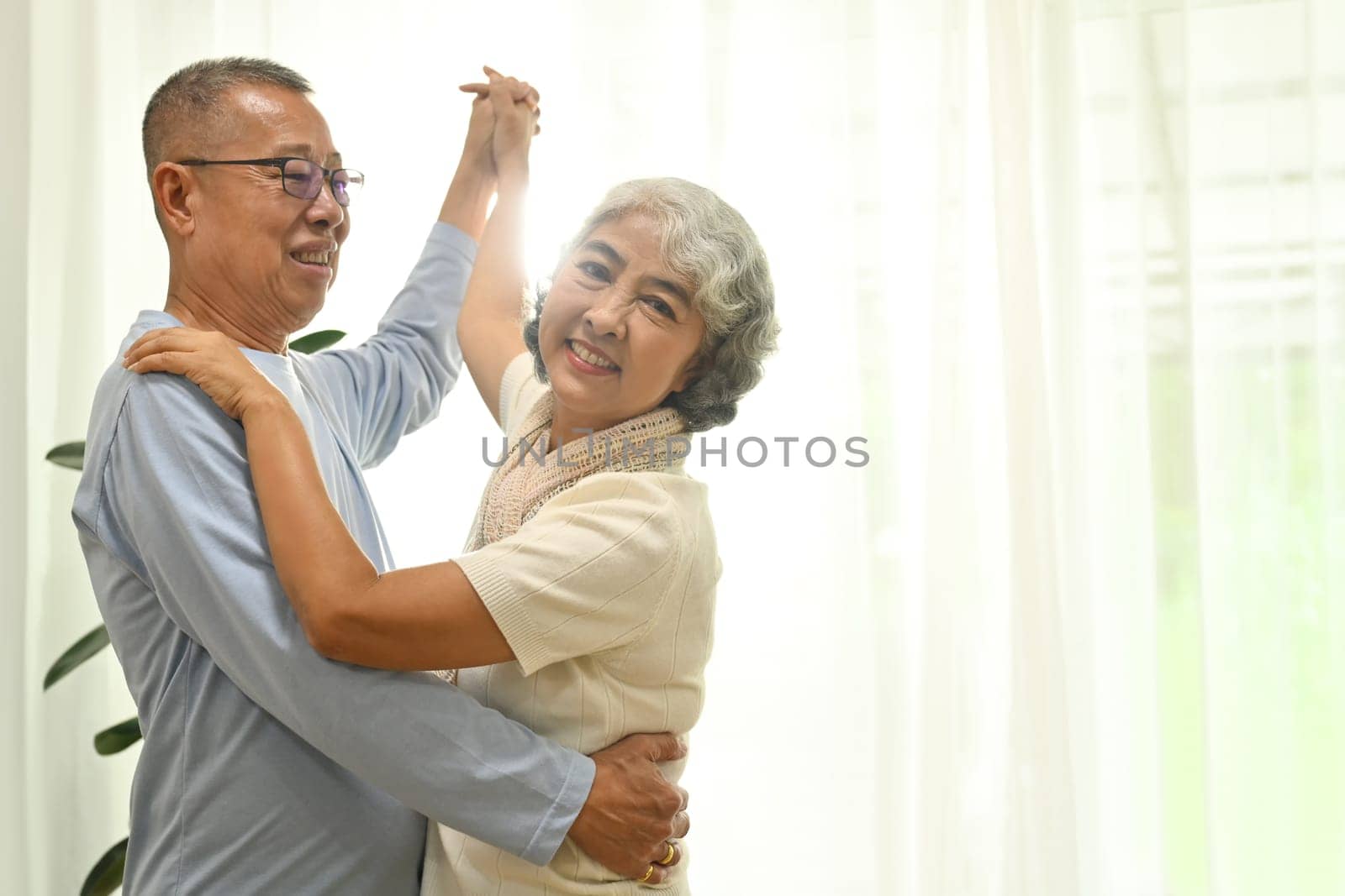 Happy elderly male and female pensioner having fun dancing in living room. Retirement lifestyle concept.