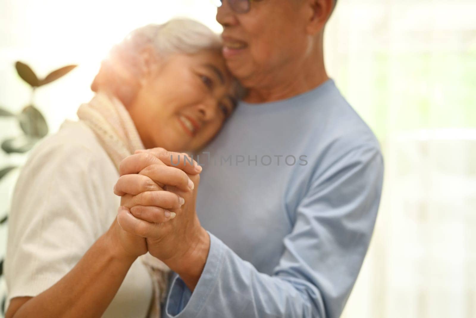 Shot of elderly couple spouses dancing in living room and looks at each other with love by prathanchorruangsak