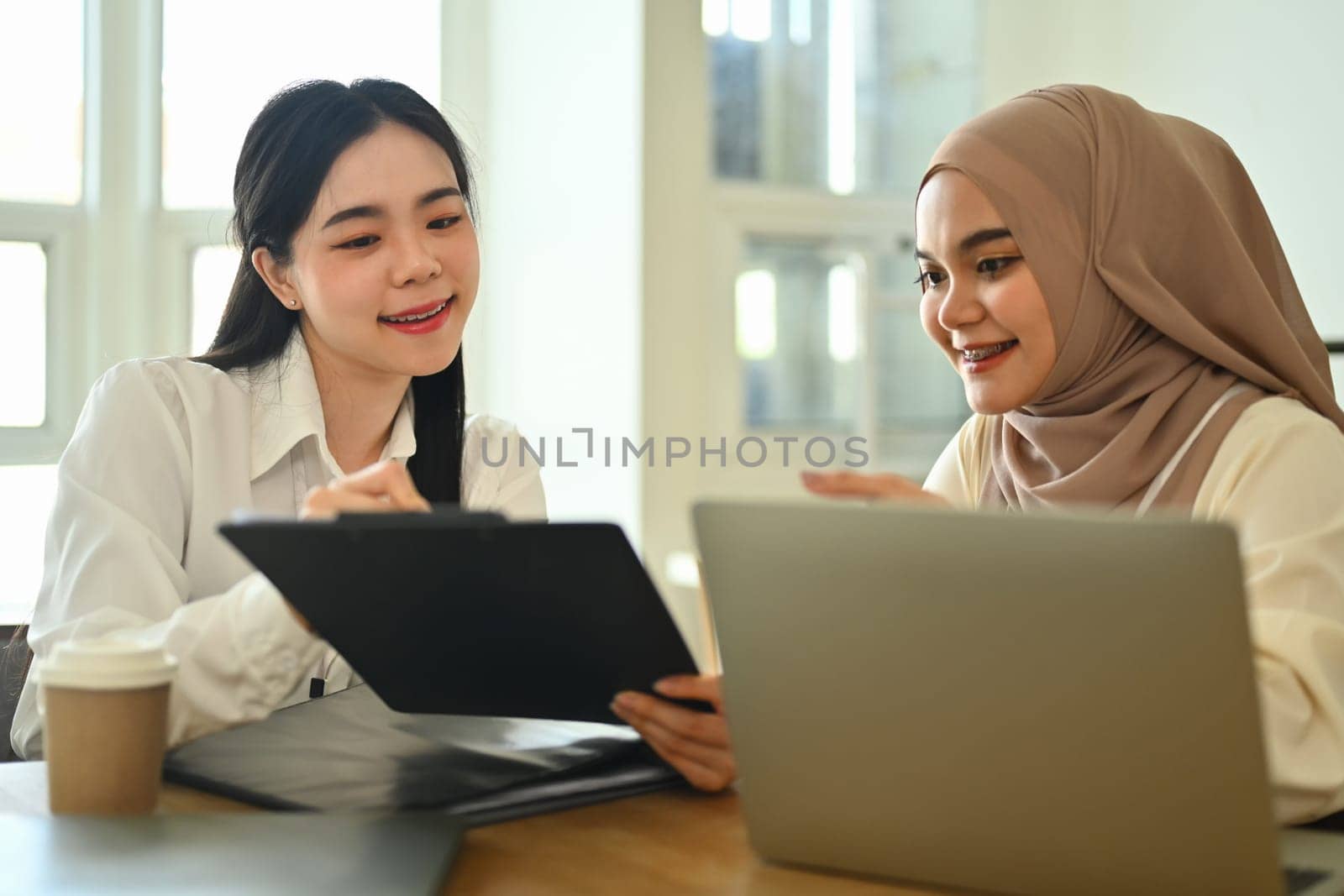 Beautiful muslim businesswoman in hijab discussing project statistics with colleague.