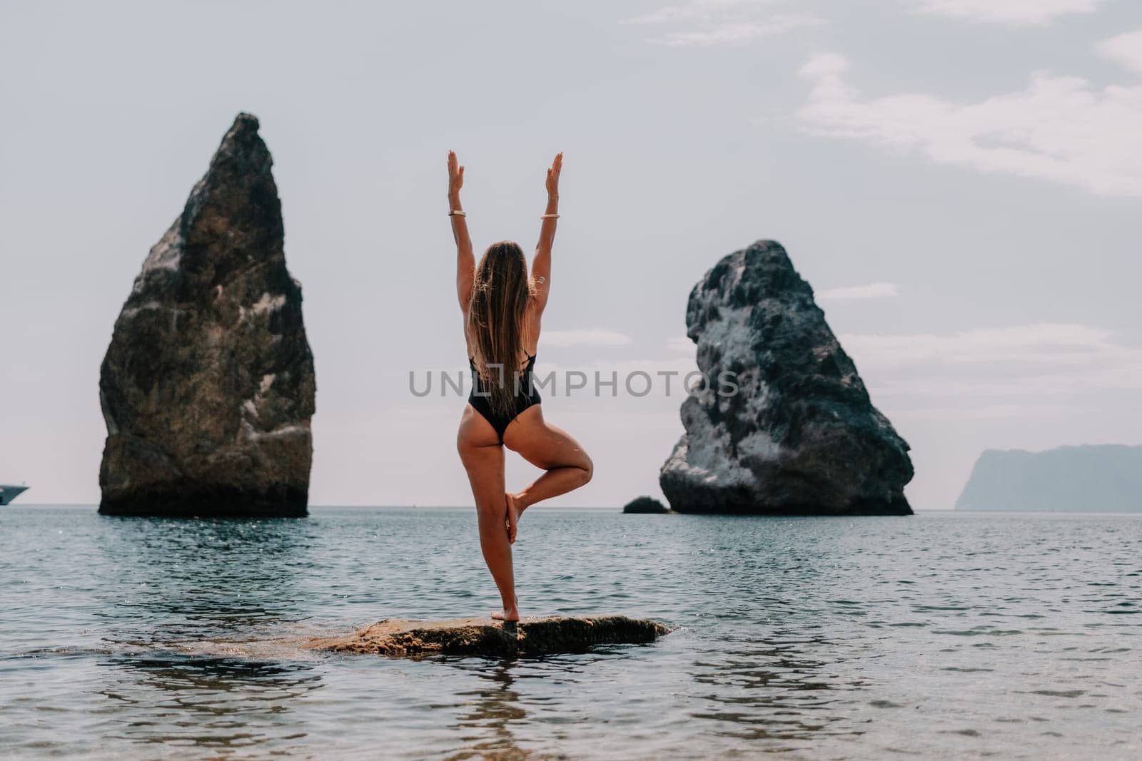 Woman sea yoga. Back view of free calm happy satisfied woman with long hair standing on top rock with yoga position against of sky by the sea. Healthy lifestyle outdoors in nature, fitness concept. by panophotograph