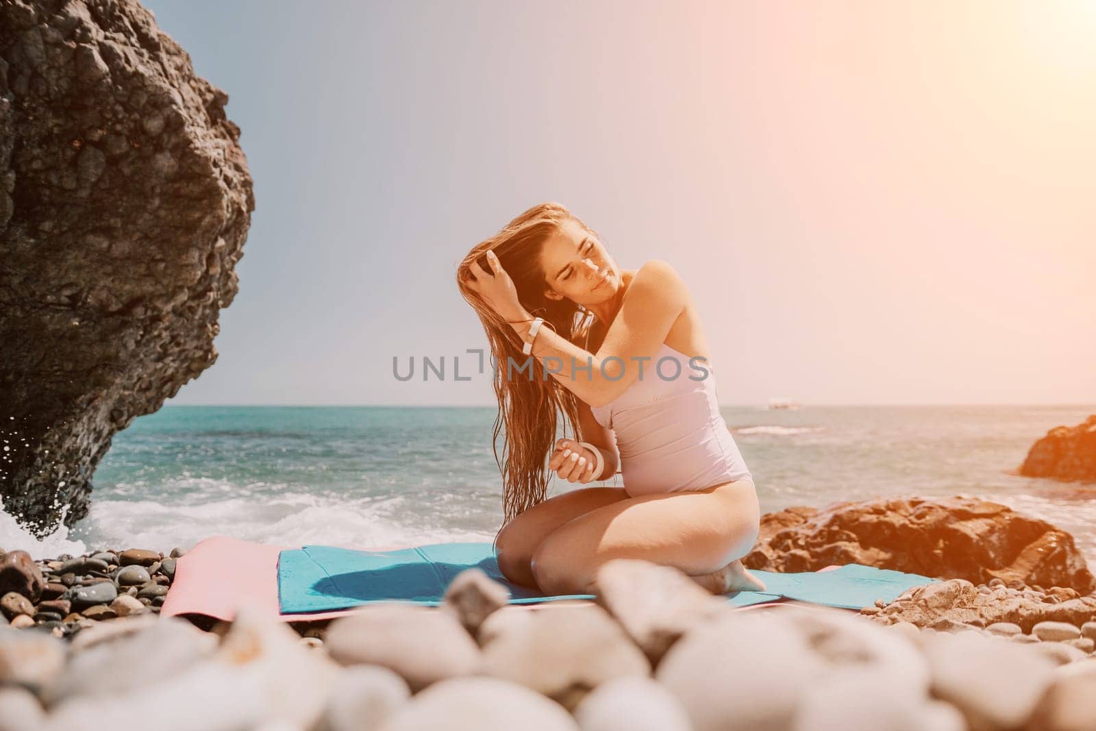 Woman sea fitness. Happy woman with long hair, fitness instructor in white bikini doing stretching and pilates on yoga mat near the sea. Female fitness yoga routine concept. Healthy lifestyle. by panophotograph