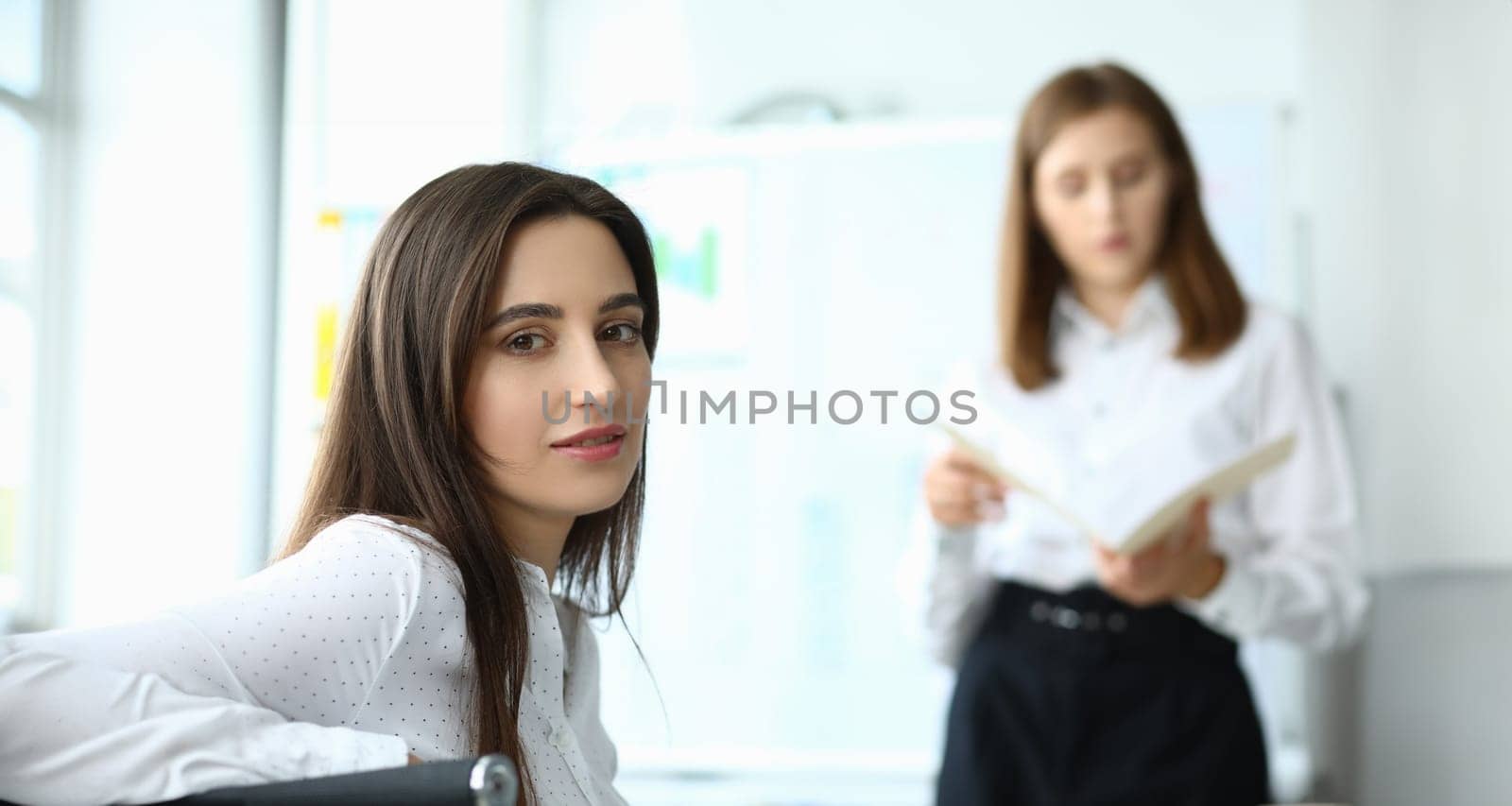 Portrait of smart businesswoman sitting at modern workplace and looking at camera with calmness. Joyful lady discussing important charts and graphs. Accounting office concept
