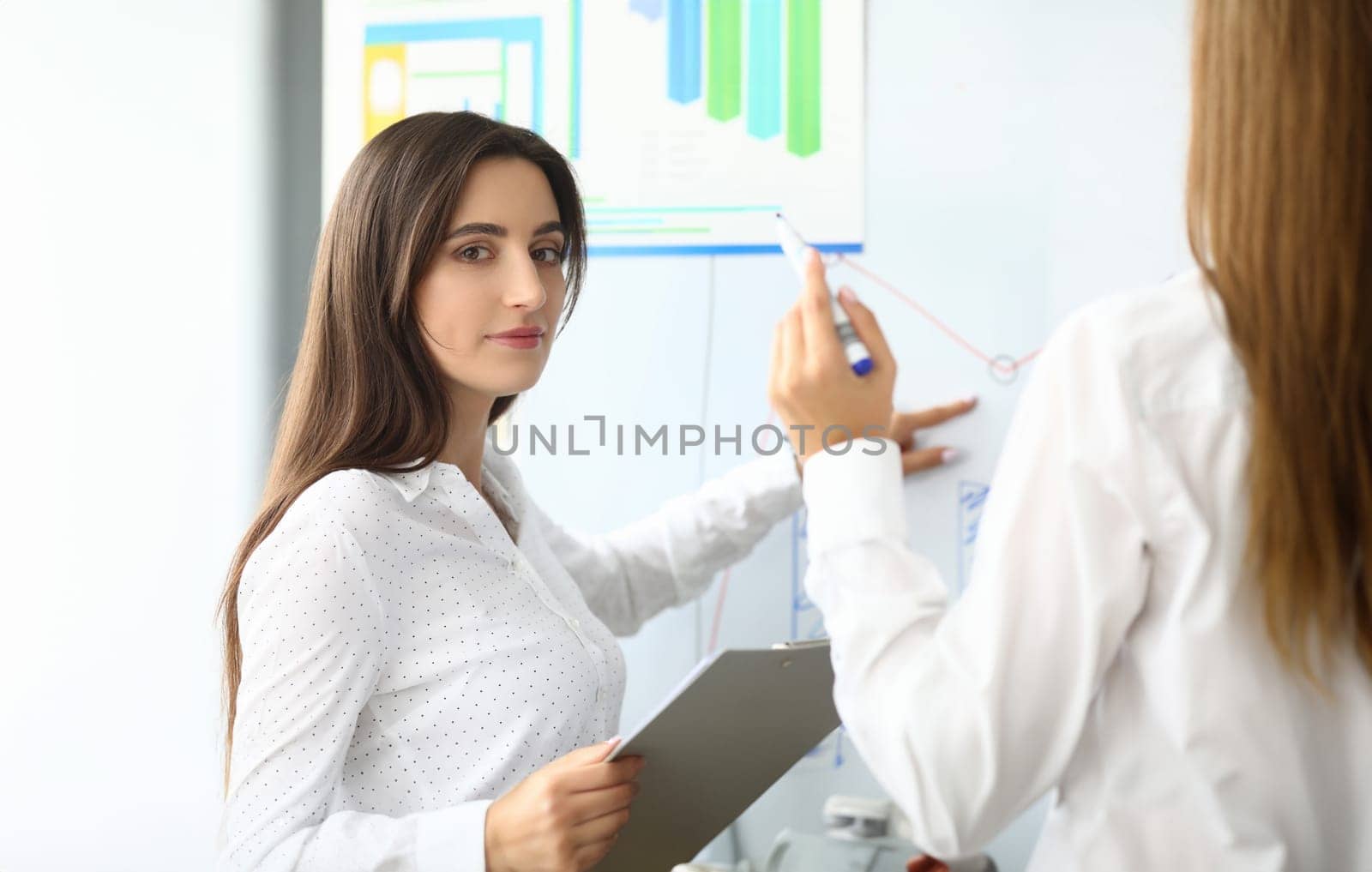 Portrait of smart businesswoman sitting in modern workplace and pointing at something on modern glass board with tender hand. Accounting office concept