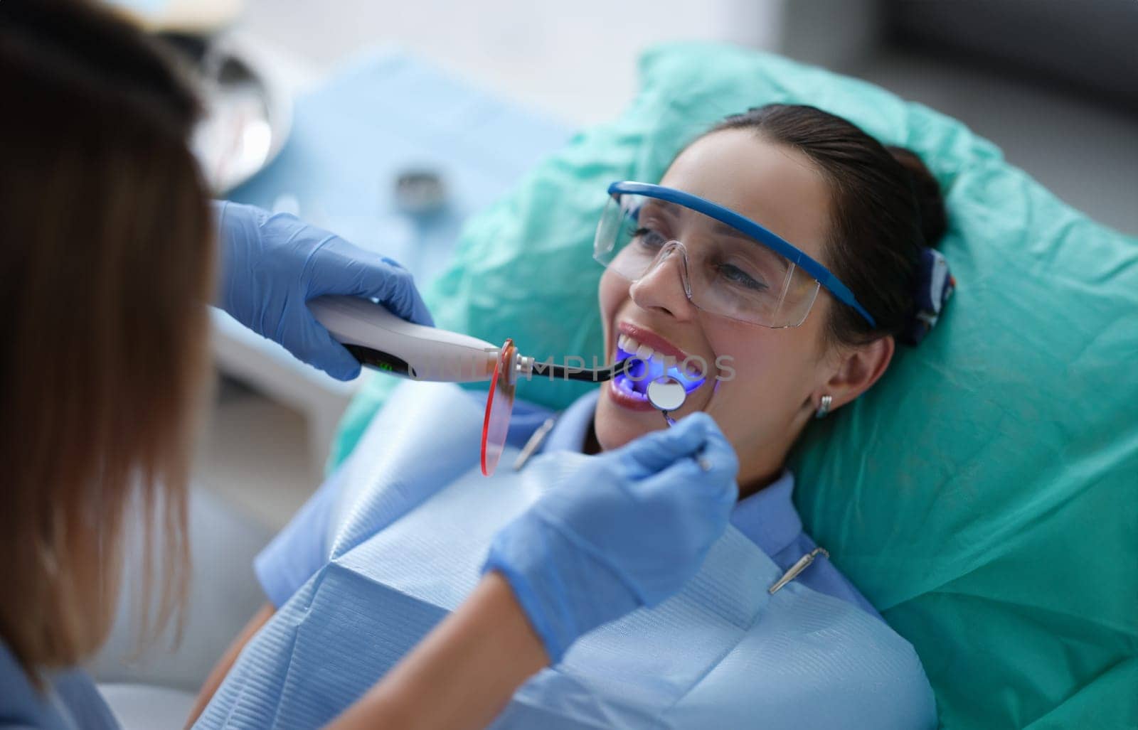 Young woman dentist in protective gloves checking dental seal, fixing photopolymer lamp during stomatology procedure by kuprevich