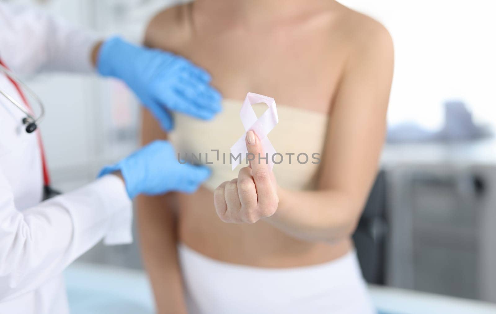 Gynecologist conducts medical examination of female breast. Woman holding pink ribbon in hand concept