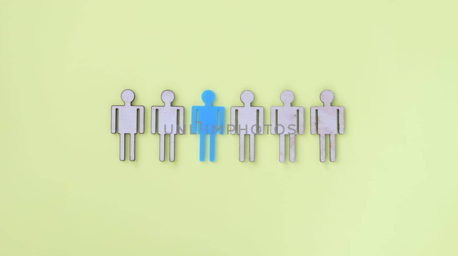 Figures of beige wooden little men in middle one blue. Human personality concept