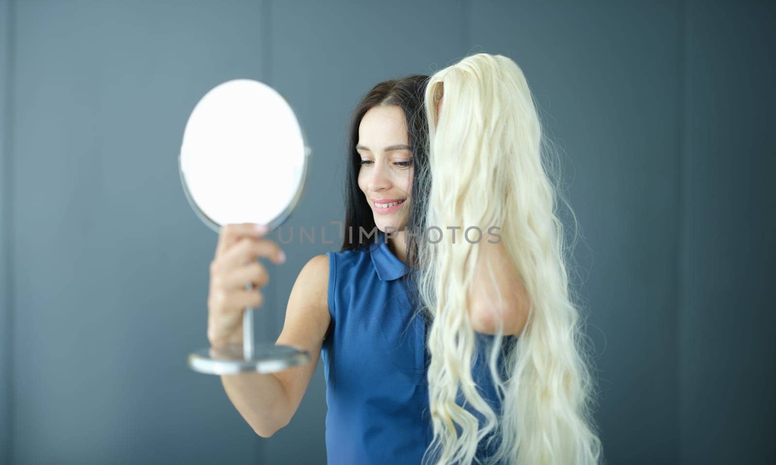 Brunette woman looks in mirror and tries on blonde wig. Choice of hair color