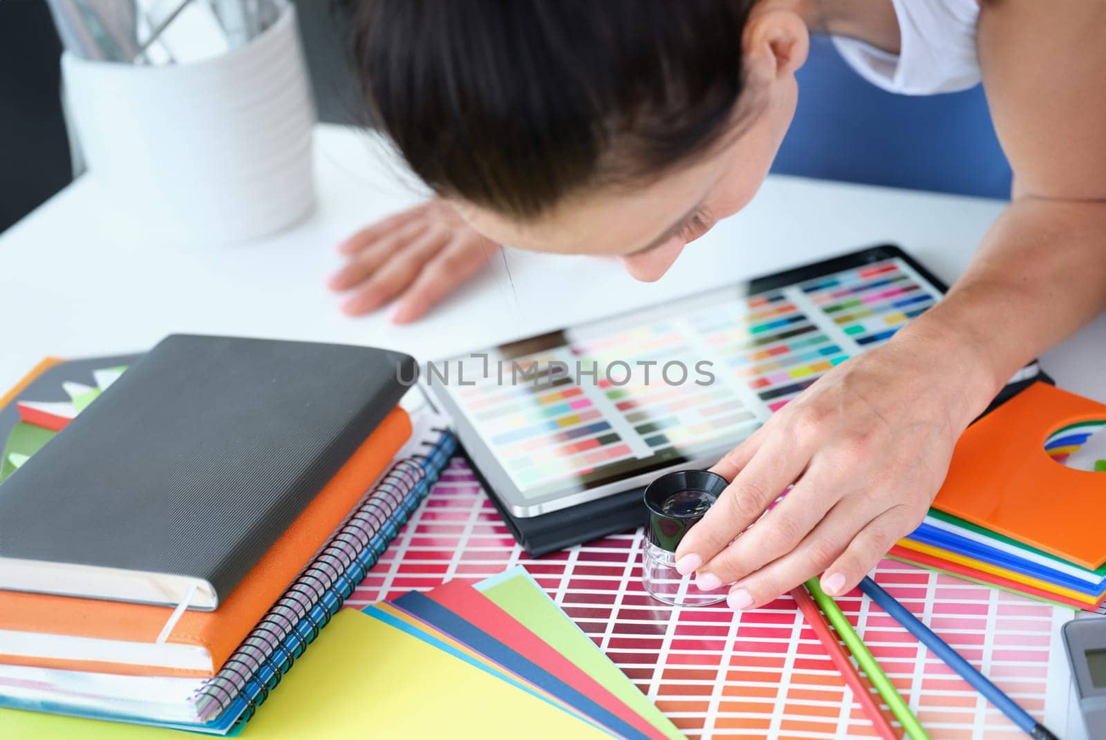 Woman designer looks through magnifying glass at color palette with different shades of colors. Color matching concept