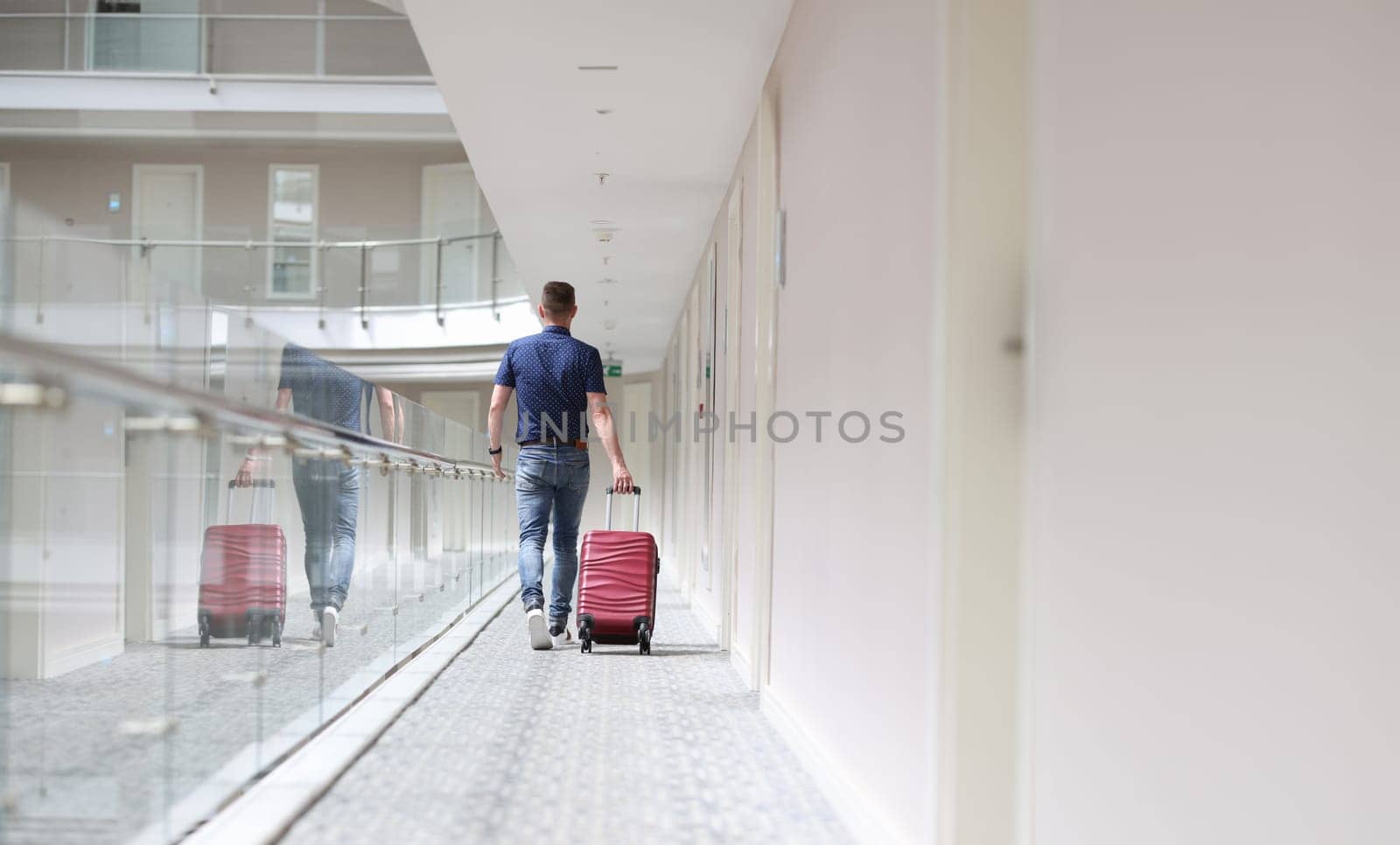 Man with suitcase walking down in hotel corridor back view. Rest in tourist hotel concept