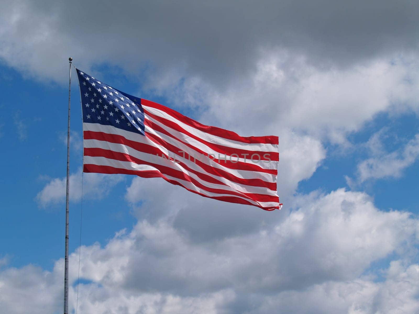 The US American red, white and blue flag flying in front of a blue cloudy sky.