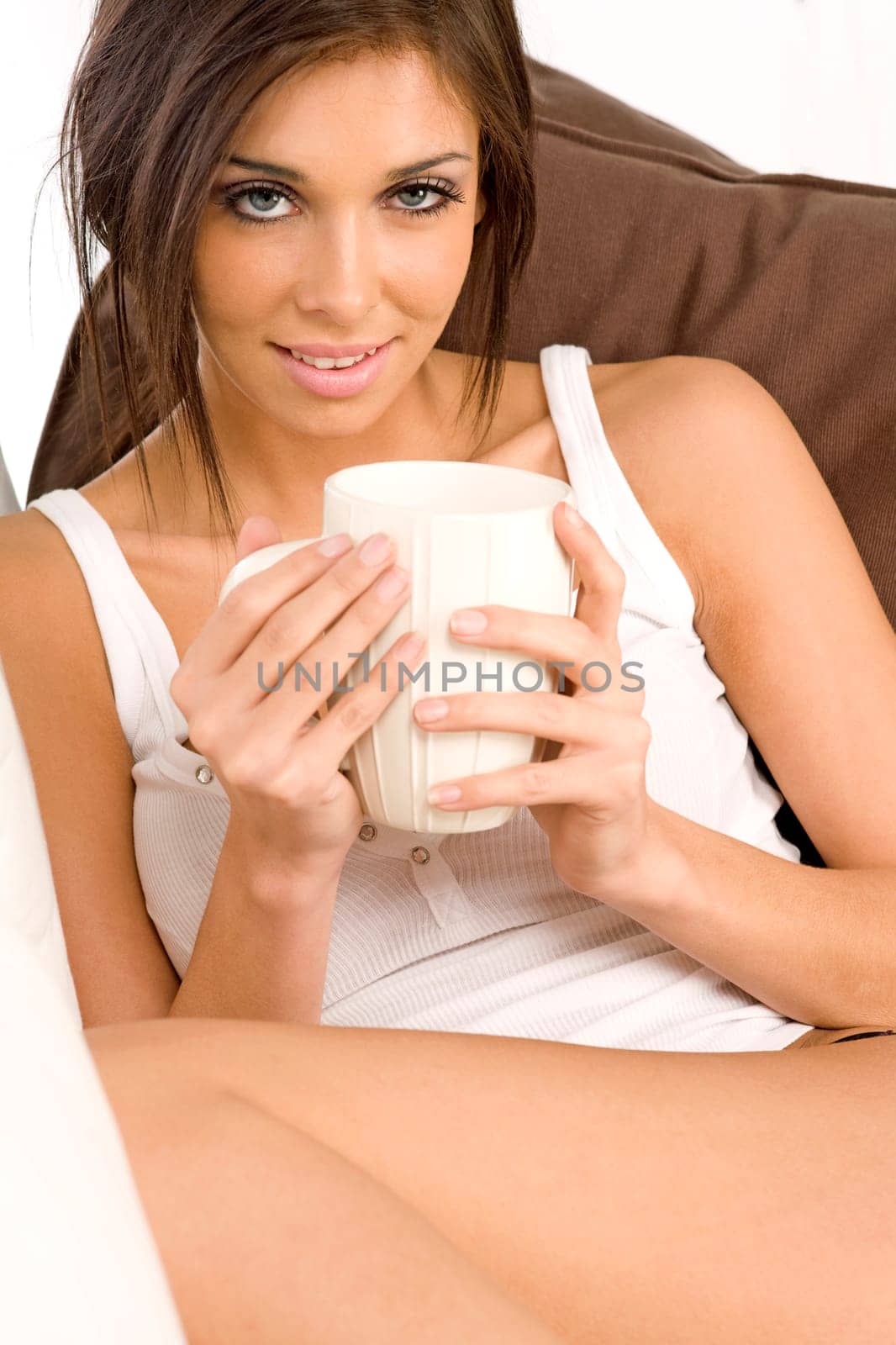 Young female resting on sofa in white vest top, dring from a mug.