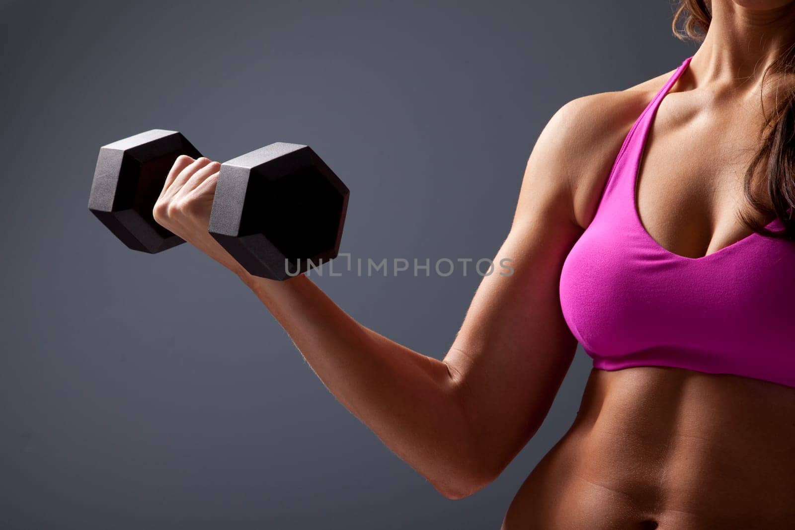 Studio close up photo of young woman lifting dumbbell.
