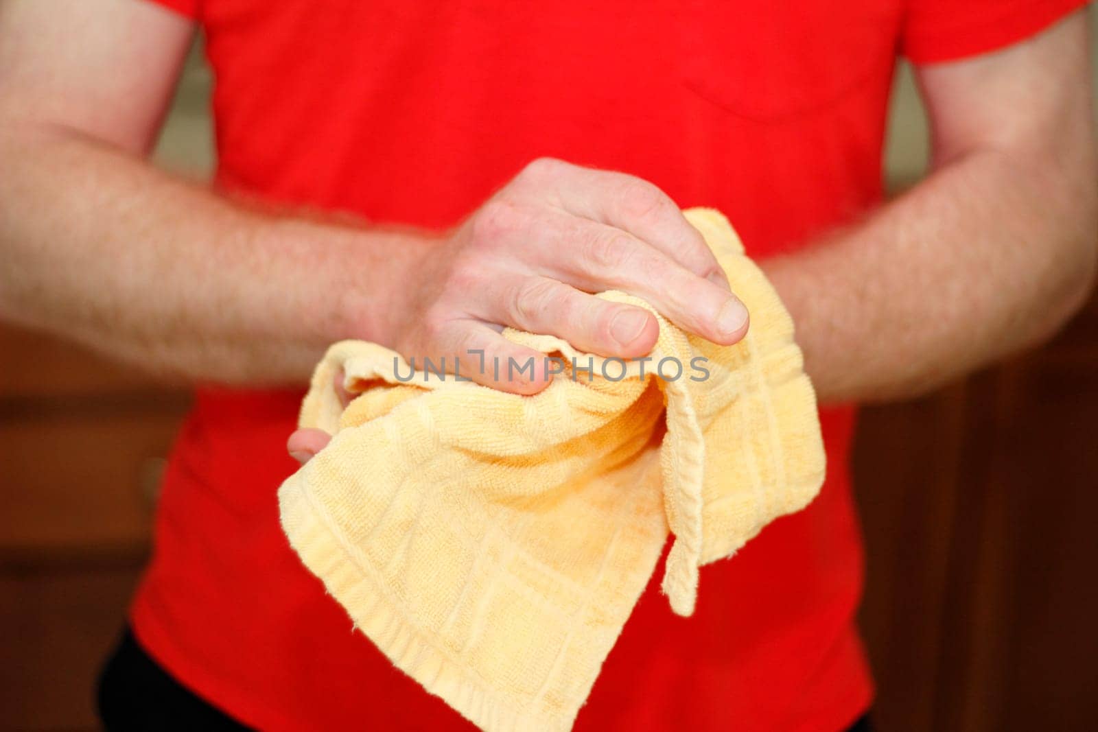 Adult male caucasian wearing a red shirt drying hands on a yellow cotton cloth dish towel close up.