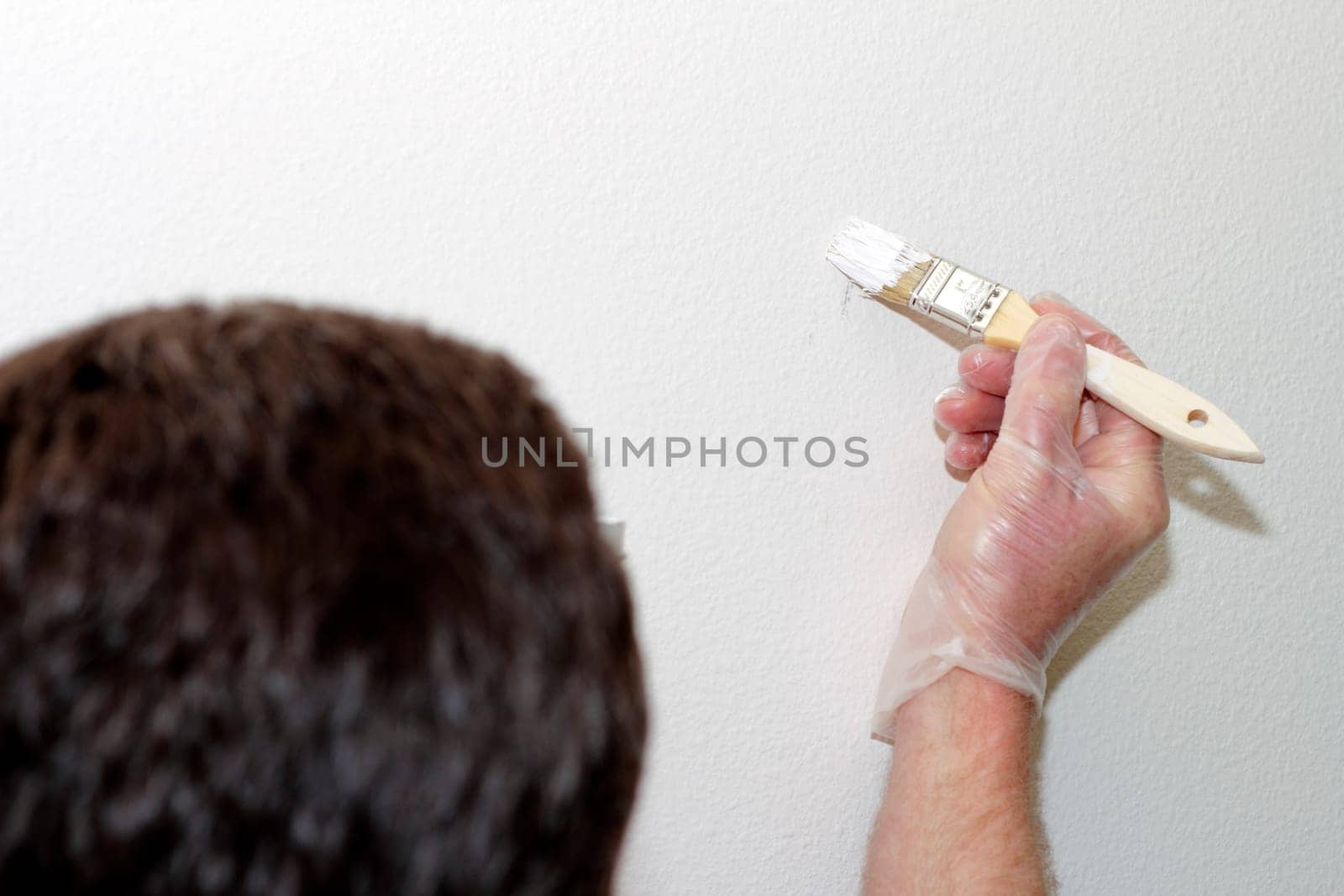Man wearing a vinyl glove painting white touch up paint with a small brush on a small spot on a wall.