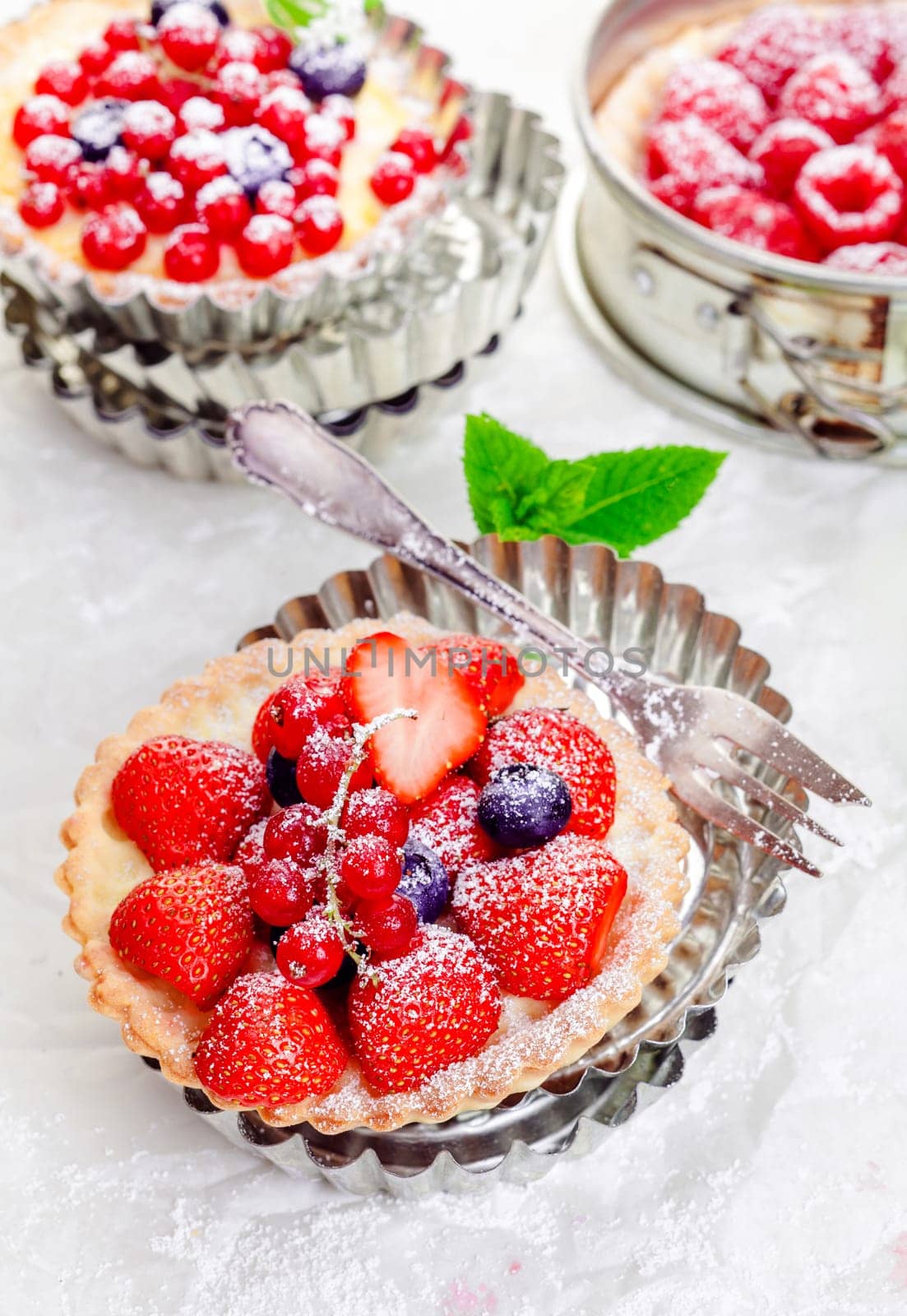 Gourmet fresh fruit mixed berry tartlets on crisp golden pie crusts served in individual decorative fluted metal pie pans