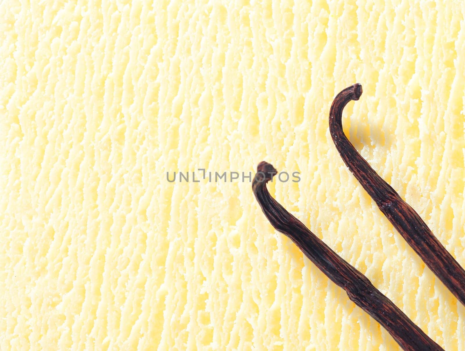 Closeup of a creamy icecream texture with two dried vanilla pods used as a flavouring during preparation