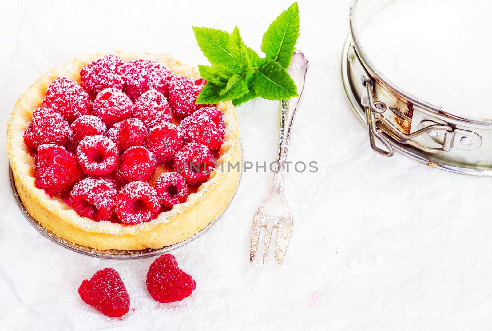 High angle view of a delicious freshly baked raspberry pie in a golden pie crust garnished with a sprig of mint and served with a silver fork