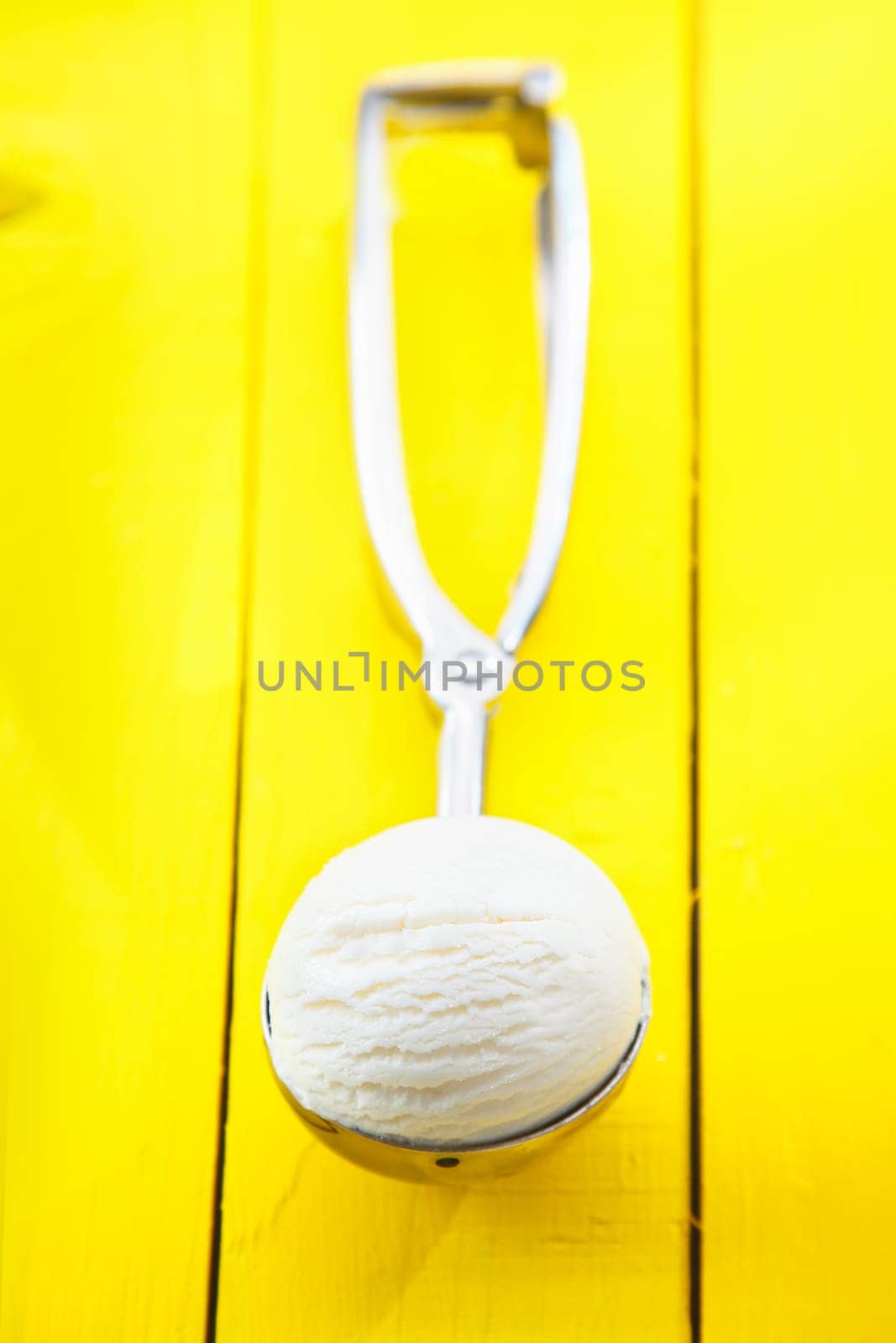 High angle view of a ball of refreshing lemon sorbet icecream served in a metal scoop on a yellow tabletop