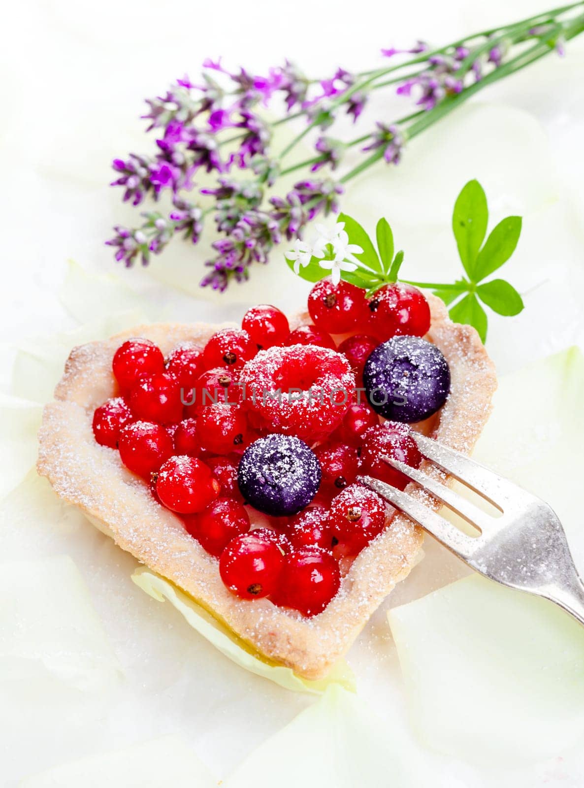 Heart-shaped redcurrant tartlet with fresh whole fruit frosted with sugar and served with a silver cake fork