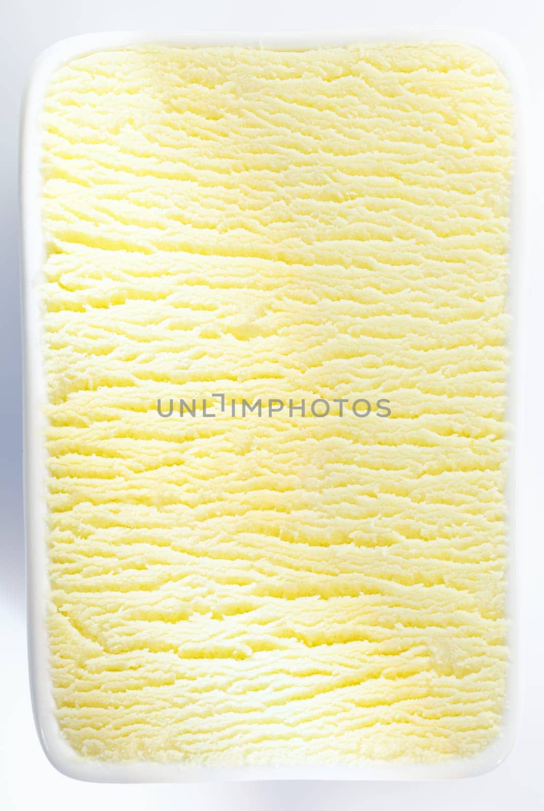 Closeup vertical background texture of a tub of lemon sorbet or vanilla icecream with a shadowed ripple running through the centre
