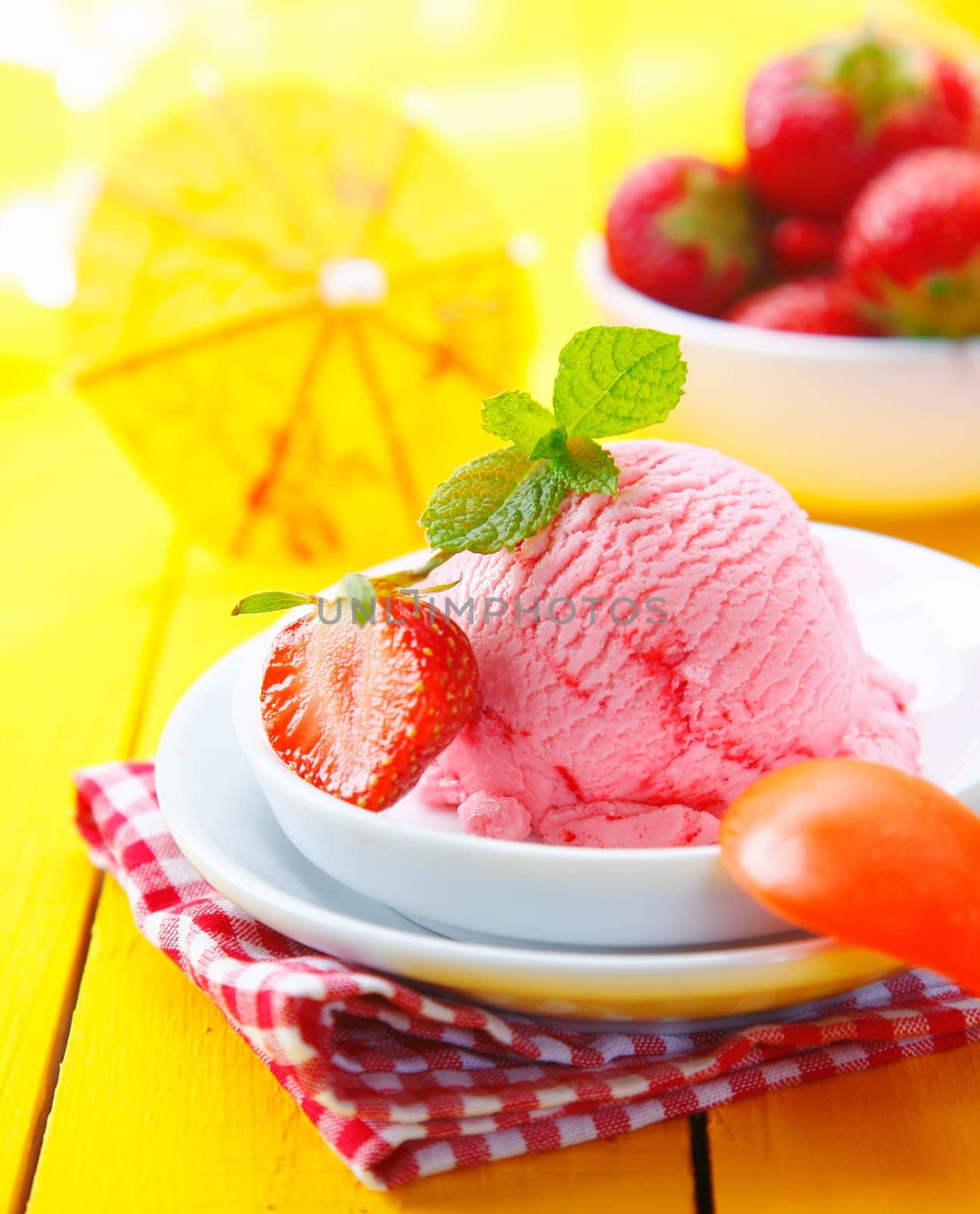 Tropical vacation icecream dessert garnished with mint and fresh strawberry served in the bright sunshine on a rustic red and white checkered napkin
