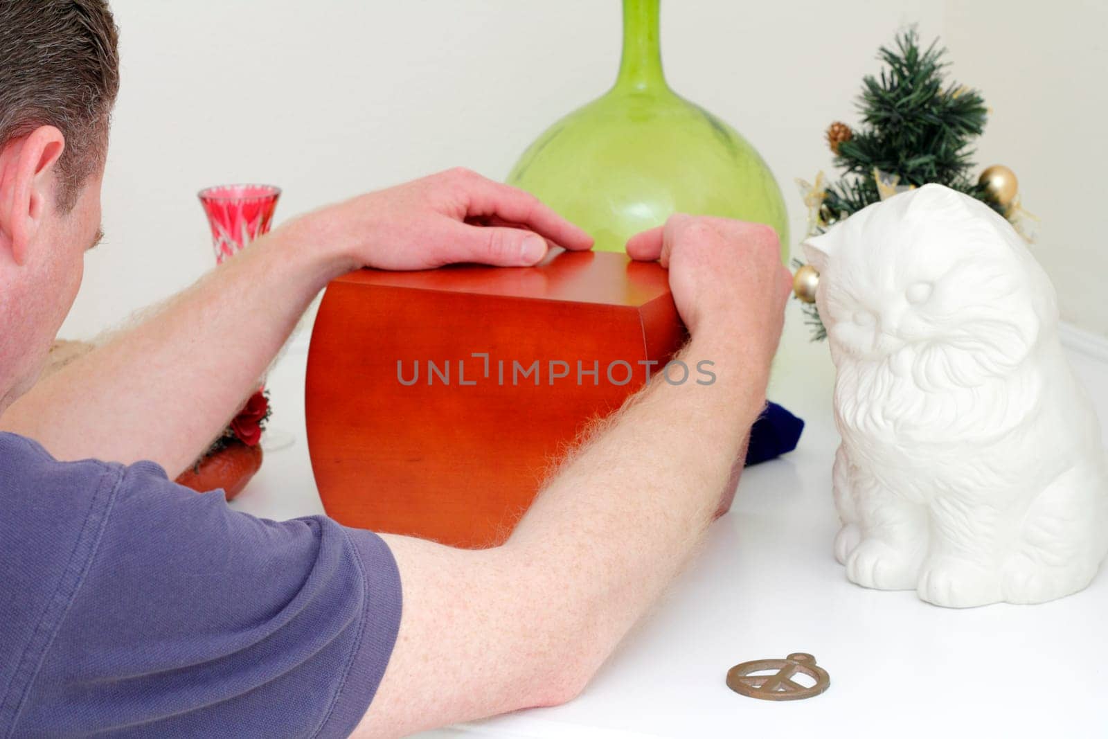 Adult male holding onto a wood urn with both hands remembering his partner who recently died. Mementoes are around the urn.