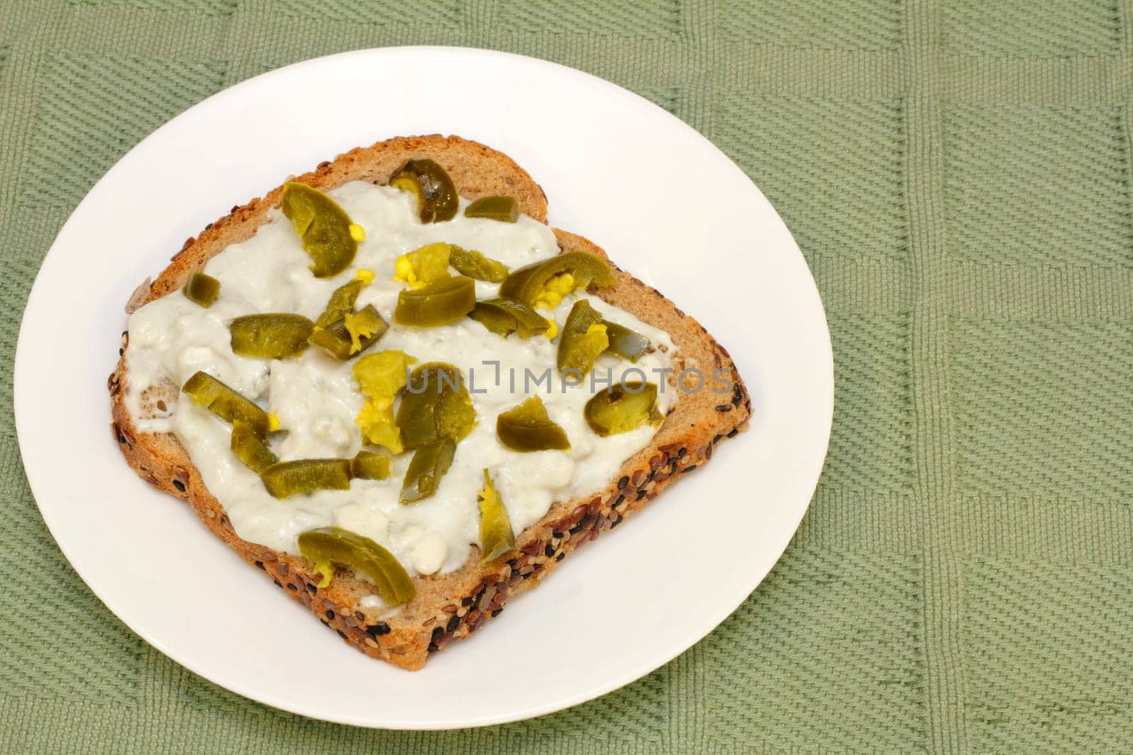 Tamed jalapeno pieces on top of blue cheese and gorgonzola spread on one sprouted grain sesame bread slice.