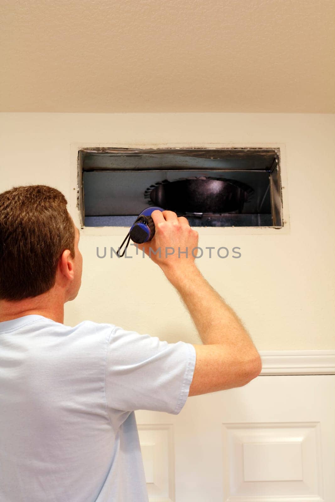 Adult male shining a flashlight into an air duct return vent to check for any need of cleaning dust or any other maintenance.